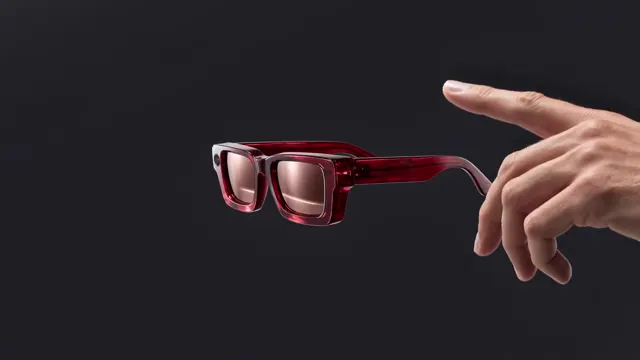 Red-framed glasses beside an extended hand against a dark product-shot background